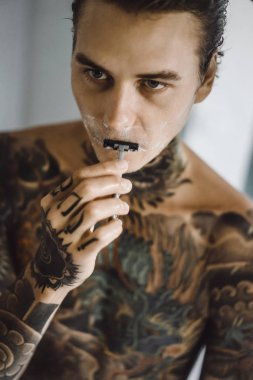 bir ayna, onun elinde bir tıraş jilet önünde genç bir yakışıklı dövmeli adam sabah tıraş.