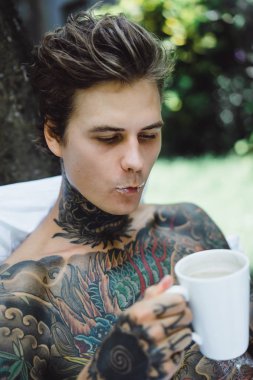 Genç yakışıklı adam açık havada bahçede açık havada yatakta kahvaltı dövme