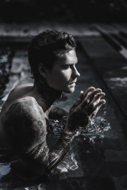 Açık Yüzme havuzunda dinlenme dövmeler genç yakışıklı adam. Dövmeli bir adam havuzda eğleniyor. Bali, Endonezya