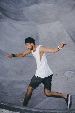 Bir havuzda pateni bir şık genç adam bir skatepark, bir kaykay üzerinde beyaz bir T-shirt ve şapka paten.