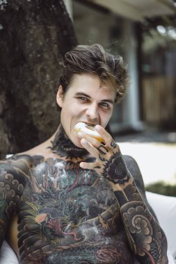 Genç yakışıklı adam açık havada bahçede açık havada yatakta kahvaltı dövme