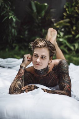 Yakışıklı genç dövmeli adam beyaz yatakta rahatlatıcı