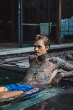 Açık Yüzme havuzunda dinlenme dövmeler genç yakışıklı adam. Dövmeli bir adam havuzda eğleniyor. Bali, Endonezya