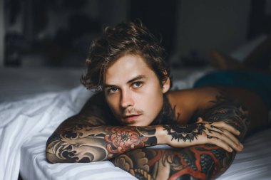 Yakışıklı genç dövmeli adam beyaz yatakta rahatlatıcı