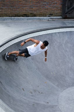Bir havuzda pateni bir şık genç adam bir skatepark, bir kaykay üzerinde beyaz bir T-shirt ve şapka paten.