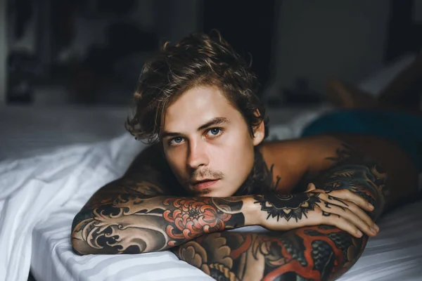 Handsome young tattooed man relaxing on white bed
