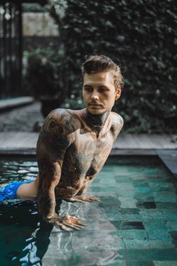 Açık Yüzme havuzunda dinlenme dövmeler genç yakışıklı adam. Dövmeli bir adam havuzda eğleniyor. Bali, Endonezya
