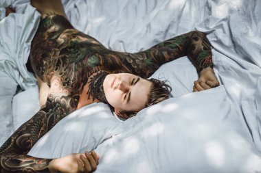 Yakışıklı genç dövmeli adam beyaz yatakta rahatlatıcı