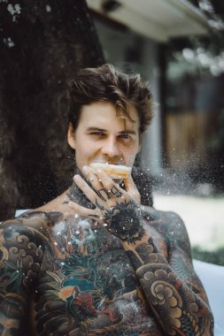 Genç yakışıklı adam açık havada bahçede açık havada yatakta kahvaltı dövme