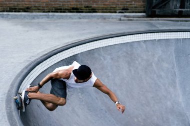 Bir havuzda pateni bir şık genç adam bir skatepark, bir kaykay üzerinde beyaz bir T-shirt ve şapka paten.