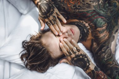 Yakışıklı genç dövmeli adam beyaz yatakta rahatlatıcı