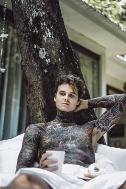 Genç yakışıklı adam açık havada bahçede açık havada yatakta kahvaltı dövme