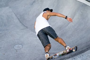 Bir havuzda pateni bir şık genç adam bir skatepark, bir kaykay üzerinde beyaz bir T-shirt ve şapka paten.
