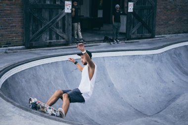 Bir havuzda pateni bir şık genç adam bir skatepark, bir kaykay üzerinde beyaz bir T-shirt ve şapka paten.