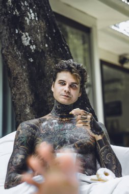 Genç yakışıklı adam açık havada bahçede açık havada yatakta kahvaltı dövme