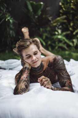 Yakışıklı genç dövmeli adam beyaz yatakta rahatlatıcı