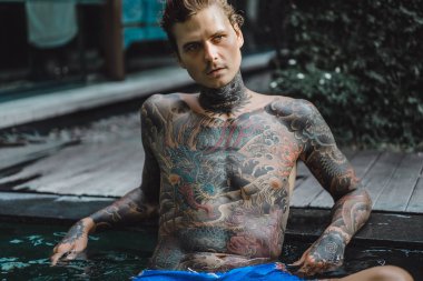 Açık Yüzme havuzunda dinlenme dövmeler genç yakışıklı adam. Dövmeli bir adam havuzda eğleniyor. Bali, Endonezya