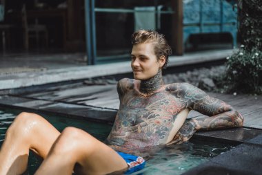 Açık Yüzme havuzunda dinlenme dövmeler genç yakışıklı adam. Dövmeli bir adam havuzda eğleniyor. Bali, Endonezya