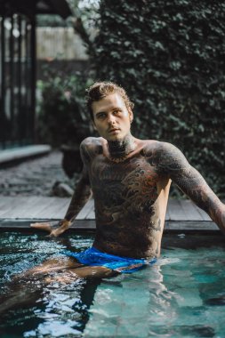 Açık Yüzme havuzunda dinlenme dövmeler genç yakışıklı adam. Dövmeli bir adam havuzda eğleniyor. Bali, Endonezya