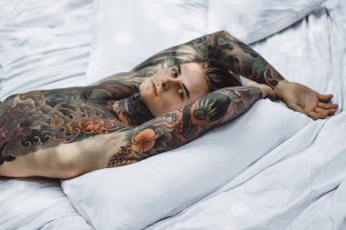 Yakışıklı genç dövmeli adam beyaz yatakta rahatlatıcı