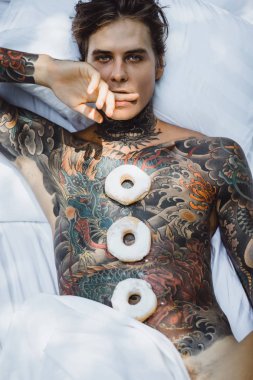 Genç yakışıklı adam açık havada bahçede açık havada yatakta kahvaltı dövme