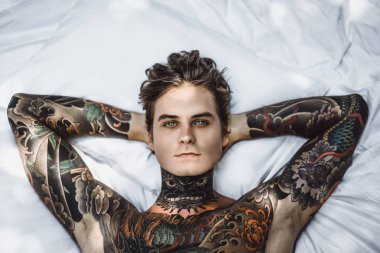 Yakışıklı genç dövmeli adam beyaz yatakta rahatlatıcı