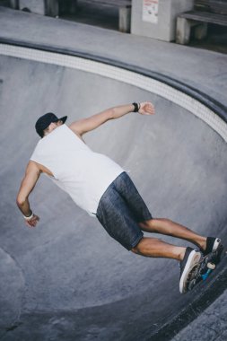 Bir havuzda pateni bir şık genç adam bir skatepark, bir kaykay üzerinde beyaz bir T-shirt ve şapka paten.