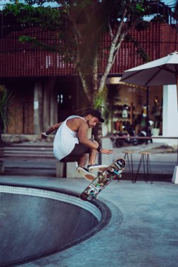 Bir havuzda pateni bir şık genç adam bir skatepark, bir kaykay üzerinde beyaz bir T-shirt ve şapka paten.