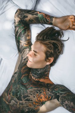 Yakışıklı genç dövmeli adam beyaz yatakta rahatlatıcı