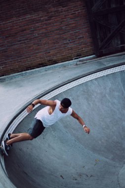 Bir havuzda pateni bir şık genç adam bir skatepark, bir kaykay üzerinde beyaz bir T-shirt ve şapka paten.