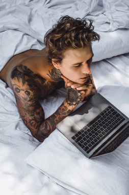 bir dizüstü bilgisayarda çalışan, posta kontrol, bir film seyrederken yatakta bir adam müzik