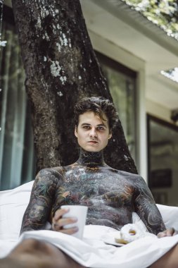 Genç yakışıklı adam açık havada bahçede açık havada yatakta kahvaltı dövme