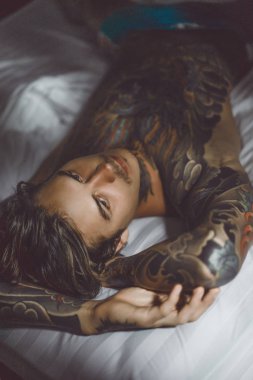 Yakışıklı genç dövmeli adam beyaz yatakta rahatlatıcı