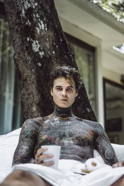 Genç yakışıklı adam açık havada bahçede açık havada yatakta kahvaltı dövme