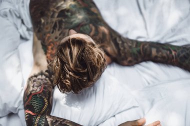 Yakışıklı genç dövmeli adam beyaz yatakta rahatlatıcı