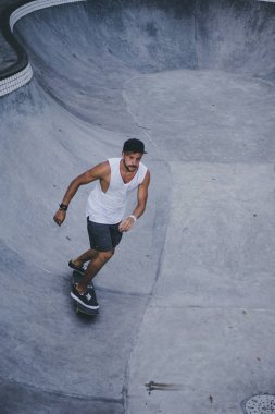 Bir havuzda pateni bir şık genç adam bir skatepark, bir kaykay üzerinde beyaz bir T-shirt ve şapka paten.