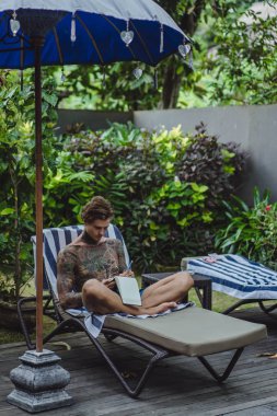 dövmeler kulaklıklar giyen genç bir erkekte müziği dinliyor ve içinde a defter bir kalem çizer. Çevrimiçi eğitim.