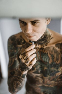 bir ayna, onun elinde bir tıraş jilet önünde genç bir yakışıklı dövmeli adam sabah tıraş.