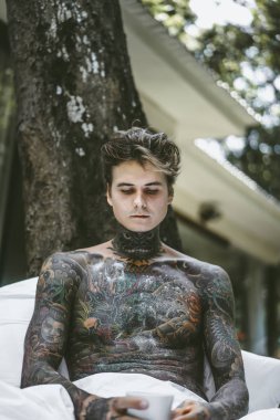 Genç yakışıklı adam açık havada bahçede açık havada yatakta kahvaltı dövme