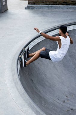 Bir havuzda pateni bir şık genç adam bir skatepark, bir kaykay üzerinde beyaz bir T-shirt ve şapka paten.