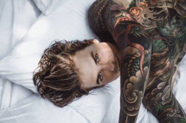 Yakışıklı genç dövmeli adam beyaz yatakta rahatlatıcı