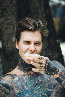 Genç yakışıklı adam açık havada bahçede açık havada yatakta kahvaltı dövme