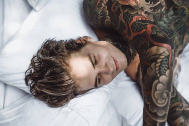 Yakışıklı genç dövmeli adam beyaz yatakta rahatlatıcı