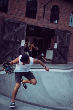 Bir havuzda pateni bir şık genç adam bir skatepark, bir kaykay üzerinde beyaz bir T-shirt ve şapka paten.