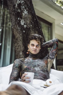 Genç yakışıklı adam açık havada bahçede açık havada yatakta kahvaltı dövme