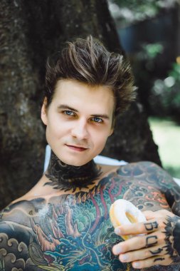 Genç yakışıklı adam açık havada bahçede açık havada yatakta kahvaltı dövme