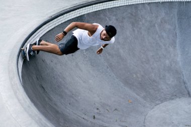 Bir havuzda pateni bir şık genç adam bir skatepark, bir kaykay üzerinde beyaz bir T-shirt ve şapka paten.