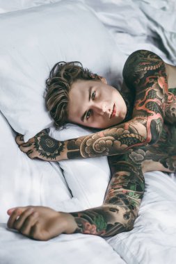 Yakışıklı genç dövmeli adam beyaz yatakta rahatlatıcı