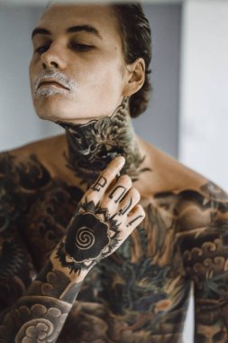 bir ayna, onun elinde bir tıraş jilet önünde genç bir yakışıklı dövmeli adam sabah tıraş.