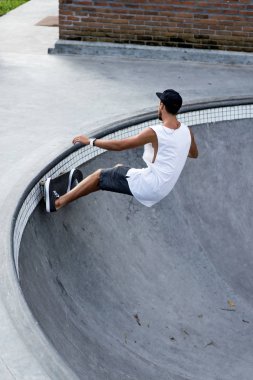 Bir havuzda pateni bir şık genç adam bir skatepark, bir kaykay üzerinde beyaz bir T-shirt ve şapka paten.